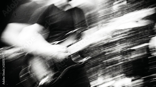 A black and white, motion-blurred close-up of a person intensely playing an electric guitar, conveying energy and movement.