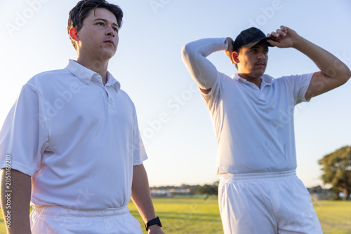 Tableau sur toile Male teammates adjusting cap and checking watch while standing on sports field i