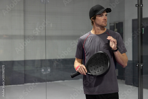 Schilderij op canvas Man standing on paddle court with glass wall wearing grey tee holding perforated