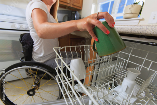 Woman with spinal cord injury in her accessible kitchen putting a cup in dishwasher
