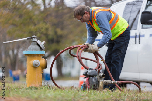 Water department technician coiling hose used to flush hydrant