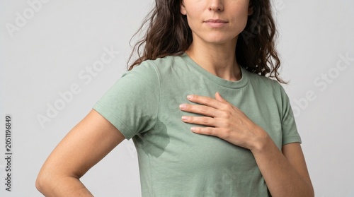 Woman wearing a sage green t-shirt with visible underarm sweat stains while standing in front of a neutral backdrop