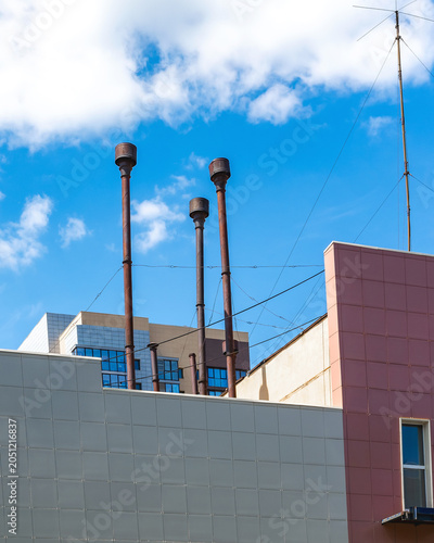 Three industrial chimneys stand on the rooftop of a building against a blue sky.