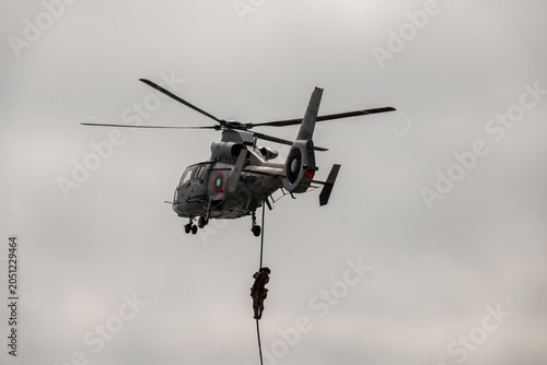 Elite special forces operator fast-roping from a hovering military helicopter during a tactical insertion or rescue mission