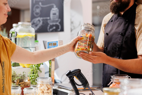 Εκτύπωση καμβά Vendor at checkout counter in zero waste shop selling nutritious produce in jar to customer with green living lifestyle, client buys ethical locally grown food in local neighborhood store, close up