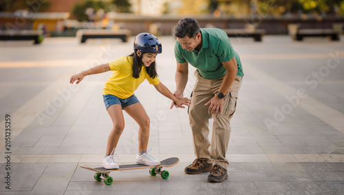 Father teaching daughter skateboarding in park with helmet