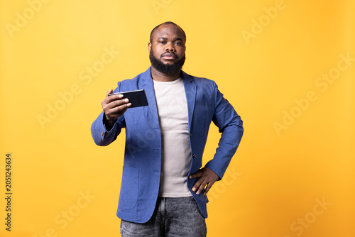 Фотография Portrait of man putting hand on hip, unhappy after receiving bad news from friend on cell phone, african American person has negative mood after reading text messages on mobile phone