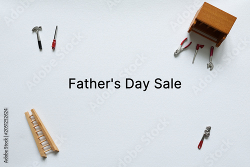 Father's Day sale message surrounded by miniature workshop tools and workbench on a white background with copy space for advertising.