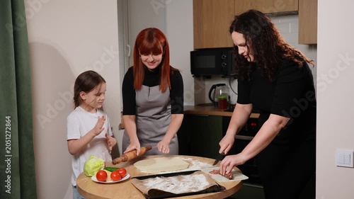 Happy family cooking homemade pizza together in kitchen. Diverse mothers with little daughter preparing fresh food. Family lifestyle, baking hobby and domestic parenting concepts, domestic lifestyle