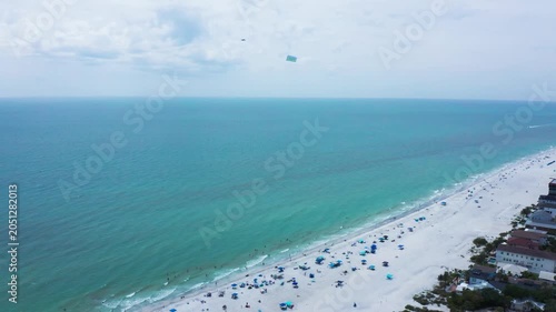 Kites hover over a serene beach with turquoise waters and scattered beachgoers. Ideal for travel content or lifestyle promotions.