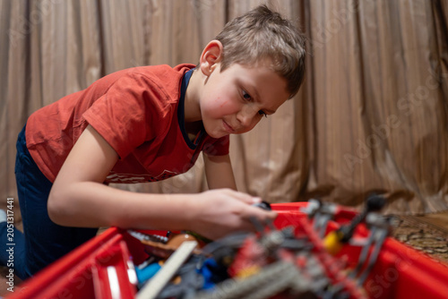 Canvas Print A focused young boy kneels indoors, intently sorting and playing with building toys from a red bin, showing concentration, creativity and quiet playtime in a cozy home environment