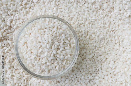 Foto A glass bowl of white Arborio rice on a surface covered in grains