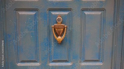 Bild auf Leinwand A close-up view of a blue painted wooden door featuring a classic brass door knocker with an integrated peephole centered on a vertical panel