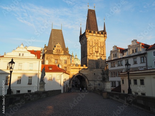 Sunrise over the iconic Charles Bridge in Prague, Czech Republic. Warm golden light illuminates the historic stone bridge and Gothic towers on the Vltava River, creating a magical morning atmosphere.