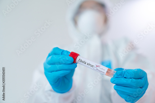 Medical Research: A gloved hand holding a vial labeled Ebola virus, with a researcher in protective gear in the background, symbolizing scientific exploration and health crisis mitigation.