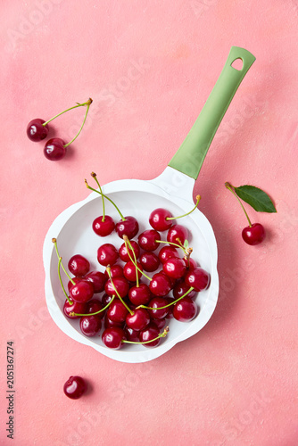 Ripe red cherries in mini frying pan on pink pastel background, top view