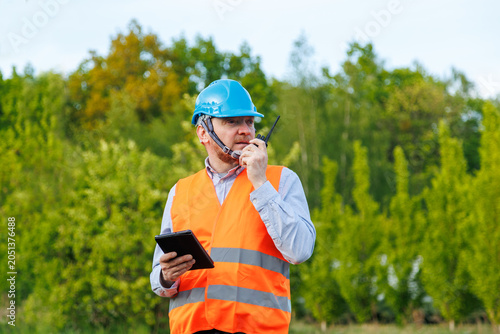 Foto Utility technician or site supervisor using a portable radio communication device during outdoor fieldwork