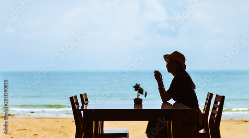 Vászonkép Single Asian young woman sits at dining table by window on tropical beach at Ao