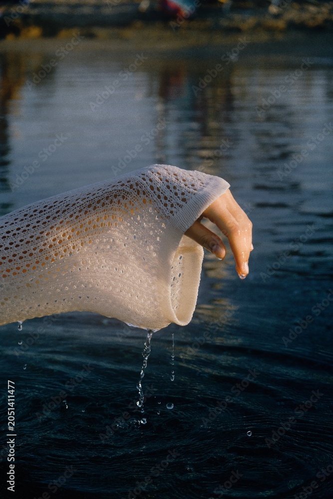 Fototapeta premium Close-up of a hand wearing a knitted glove partially submerged in dark water with visible water droplets.
