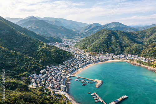 Aerial view of coastal village with harbor surrounded by green mountains and blue sea