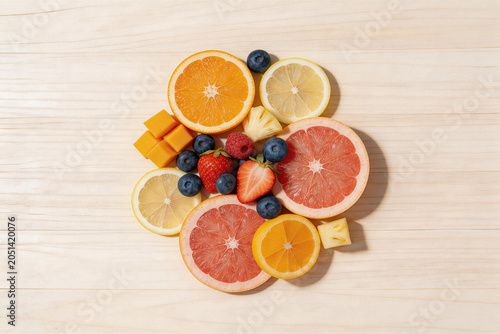 Assorted fresh citrus slices and mixed berries on light wooden background
