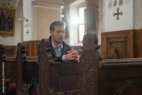 Serene man, a believer in empty Catholic church, bowing toward the altar, entering a pew, and sitting to pray.