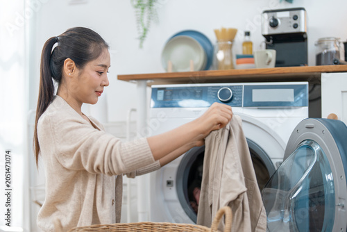Woman laundry washing machine home clothing basket appliance domestic clean chore woman loading clothing into front load washing machine in bright home laundry room with calm expression
