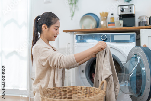 Laundry woman washing machine basket home clothing fabric appliance clean domestic, woman loading clothing into front load washer with wicker basket bright home laundry room, calm daily chore
