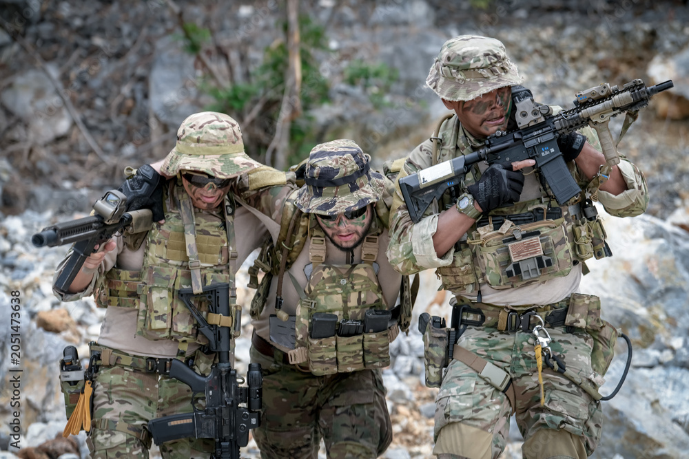 Fototapeta premium Special forces soldiers in camouflage assist a wounded comrade during a tactical training exercise