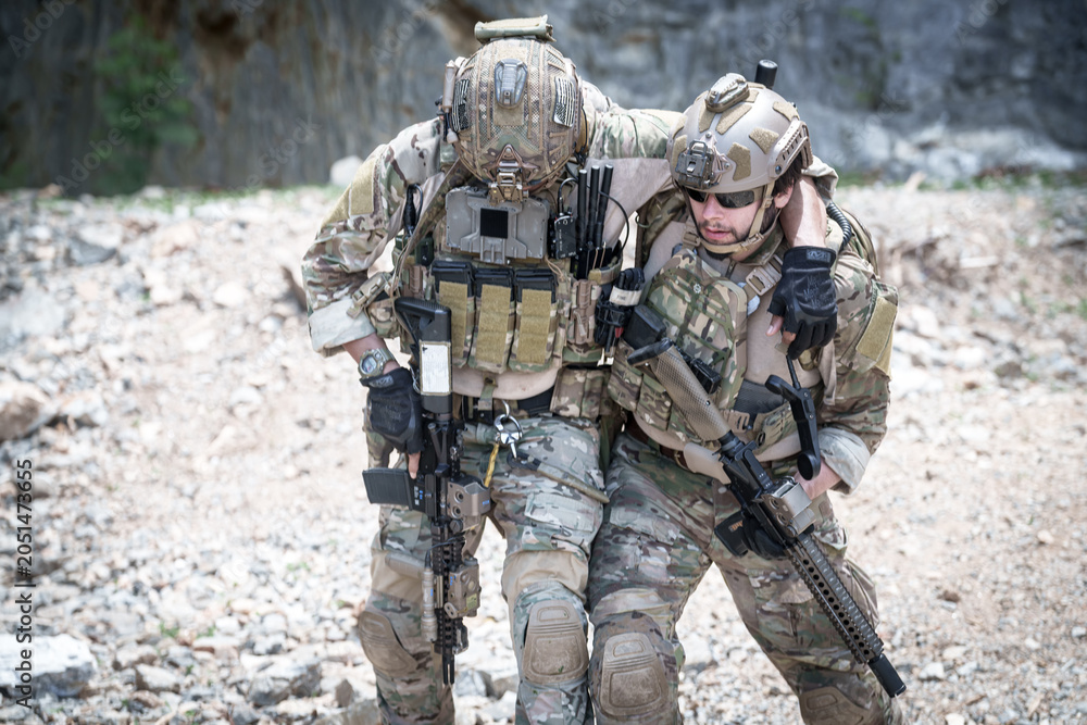 Fototapeta premium Two soldiers in tactical gear assisting each other while walking through rocky terrain