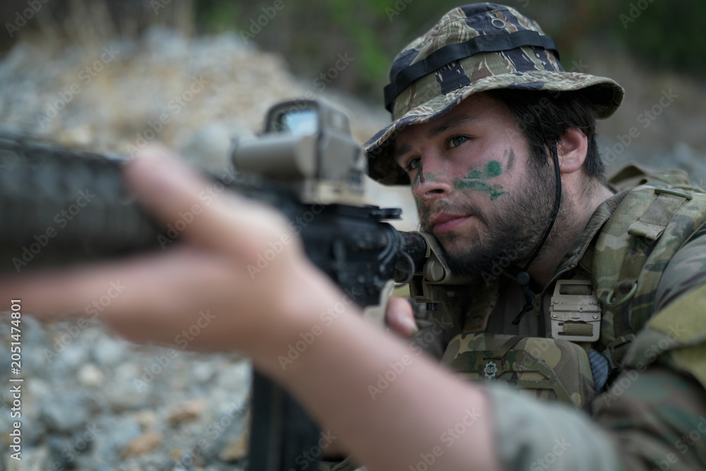 Fototapeta premium Soldier with camouflage face paint aims rifle in tactical gear during outdoor operation