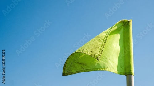 Neon golf flag ripples against clear blue sky on professional green course turf.