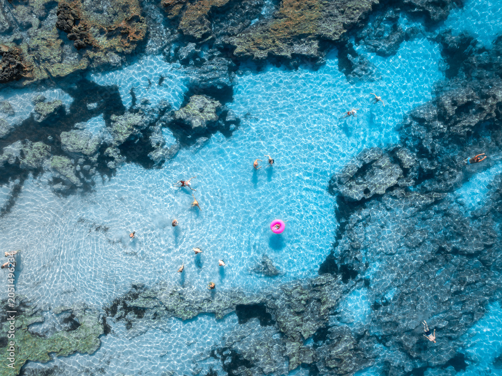 Obraz premium Aerial top down view of people swimming in crystal clear turquoise water of natural pool in rocks. Summer in Mallorca, Spain. Tourists relaxing with pink swim ring in Mediterranean sea. Drone view