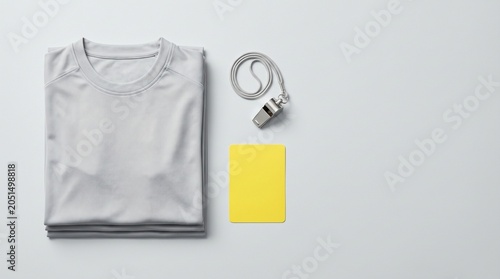 Folded gray t-shirt with whistle and yellow card on white background