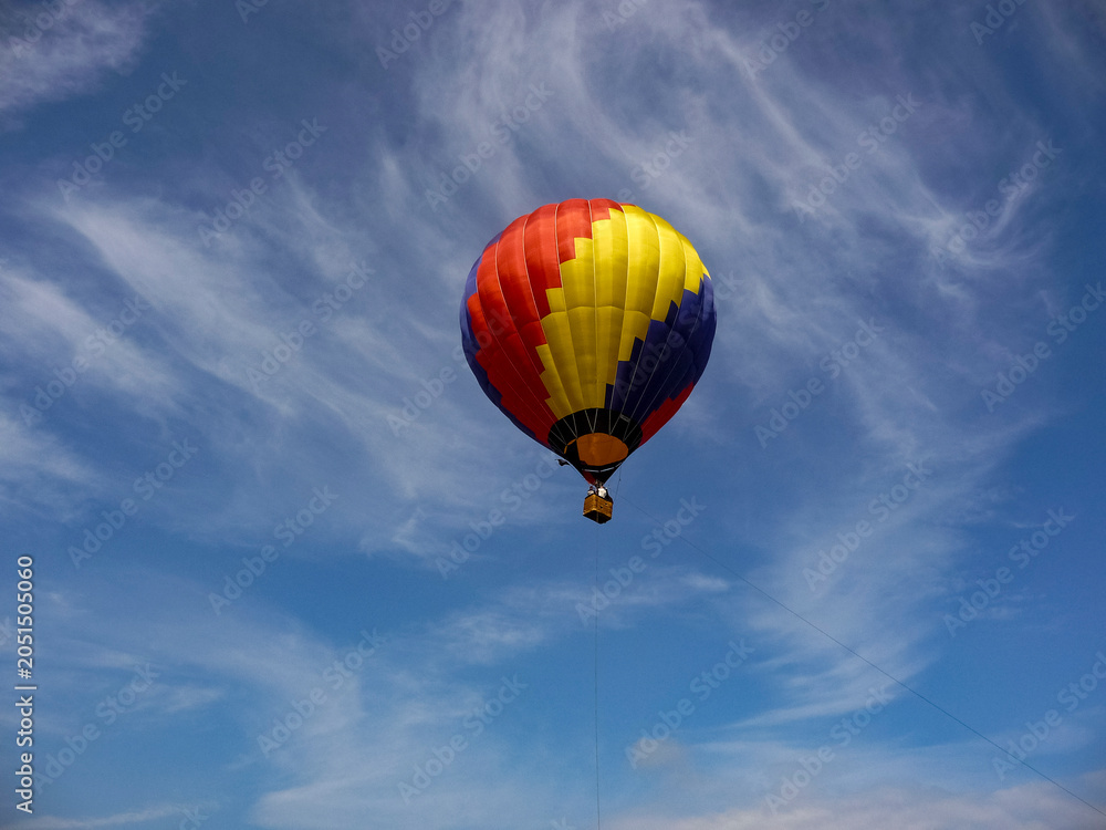 Fototapeta premium Colorful hot air balloon flying in blue sky with wispy clouds 