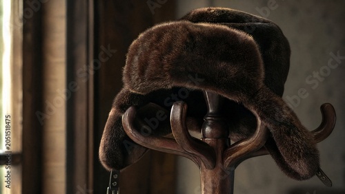 Deep brown bearskin ushanka hat resting on a dark wooden coat rack.
