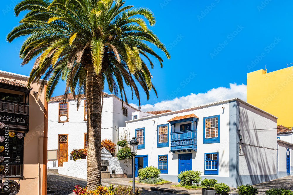 Fototapeta premium Charming cobblestone plaza is lined with white traditional buildings featuring bright blue wooden accents in Santa Cruz town, La Palma, Canary Islands, Spain