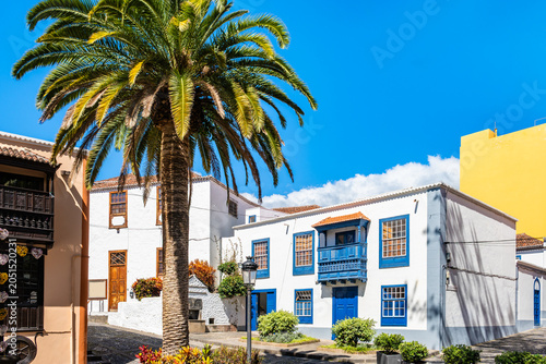 Charming cobblestone plaza is lined with white traditional buildings featuring bright blue wooden accents in Santa Cruz town, La Palma, Canary Islands, Spain