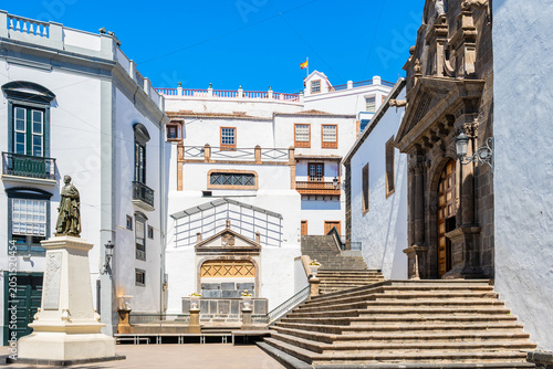 Sweeping stone staircase leads to an old church entrance next to a historic statue in a sunny plaza in Santa Cruz town, La Palma, Canary Islands, Spain