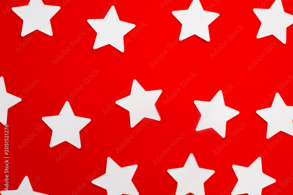 Fototapeta premium White paper stars pattern on bright red background surface top view. Flat lay composition of clean star shapes evenly distributed over vibrant colorful backdrop.
