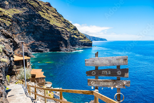 Rustic wooden signpost stands on a coastal cliff path overlooking a beautiful blue bay at Puntagorda, La Palma, Canary Islands, Spain