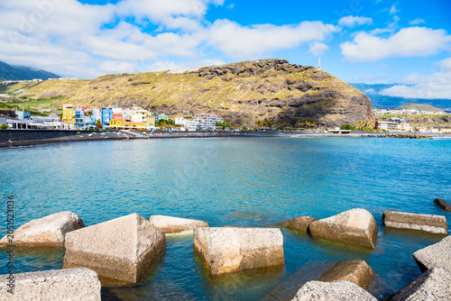 Large concrete breakwater blocks sit in clear turquoise water protecting a beach and coastal town in Tazacorte town, La Palma, Canary Islands, Spain