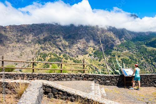 Hiker stands by a stone wall overlooking a dramatic, cloud-capped mountain range at Cancelita viewpoint, La Palma, Canary Islands, Spain