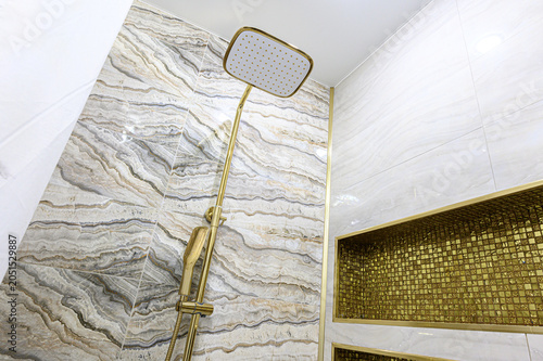 Luxurious shower zone with marble-patterned beige tiles, gold-finished fixtures, and a decorative gold mosaic niche for storage, exuding opulent elegance