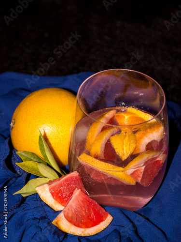 Glass filled with sliced grapefruit and a pink gin and tonic on a royal blue cloth.