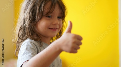 Happy young girl with long brown hair giving a thumbs up against a bright yellow wall