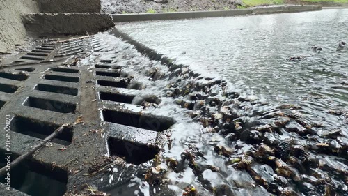 Rainwater flows rapidly through the metal grate. The rushing water creates a loud gurgling and splashing sound.