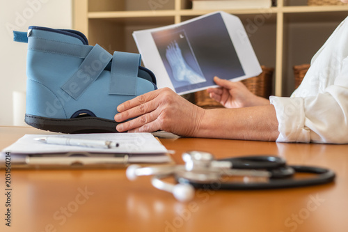Medical specialist explaining bone fracture diagnosis to patient using x-ray images and an orthopedic boot during clinic consultation for ankle or foot injury care and recovery