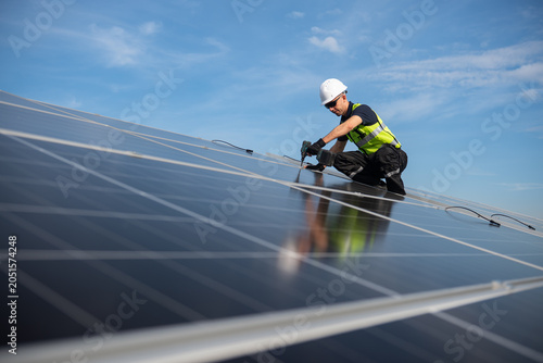Technician installing solar panels on factory roof for green energy. A skilled technician in safety gear is working on a solar panel installation on rooftop.