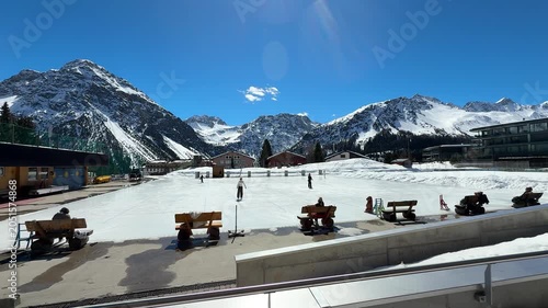 Children enjoying ice skating on a frozen lake in Arosa, Switzerland, surrounded by snowy Alpine scenery during winter.